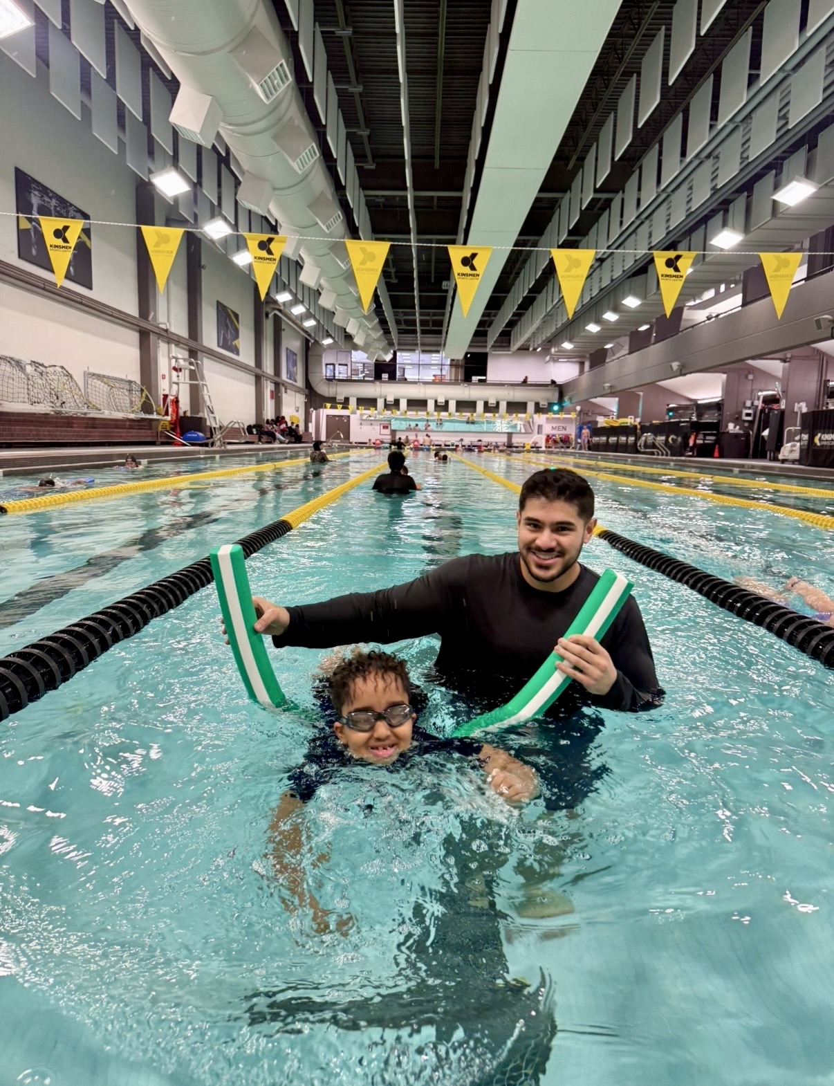 Smiling child and volunteer holding kickboards together in the pool at Kinsmen Sports Centre