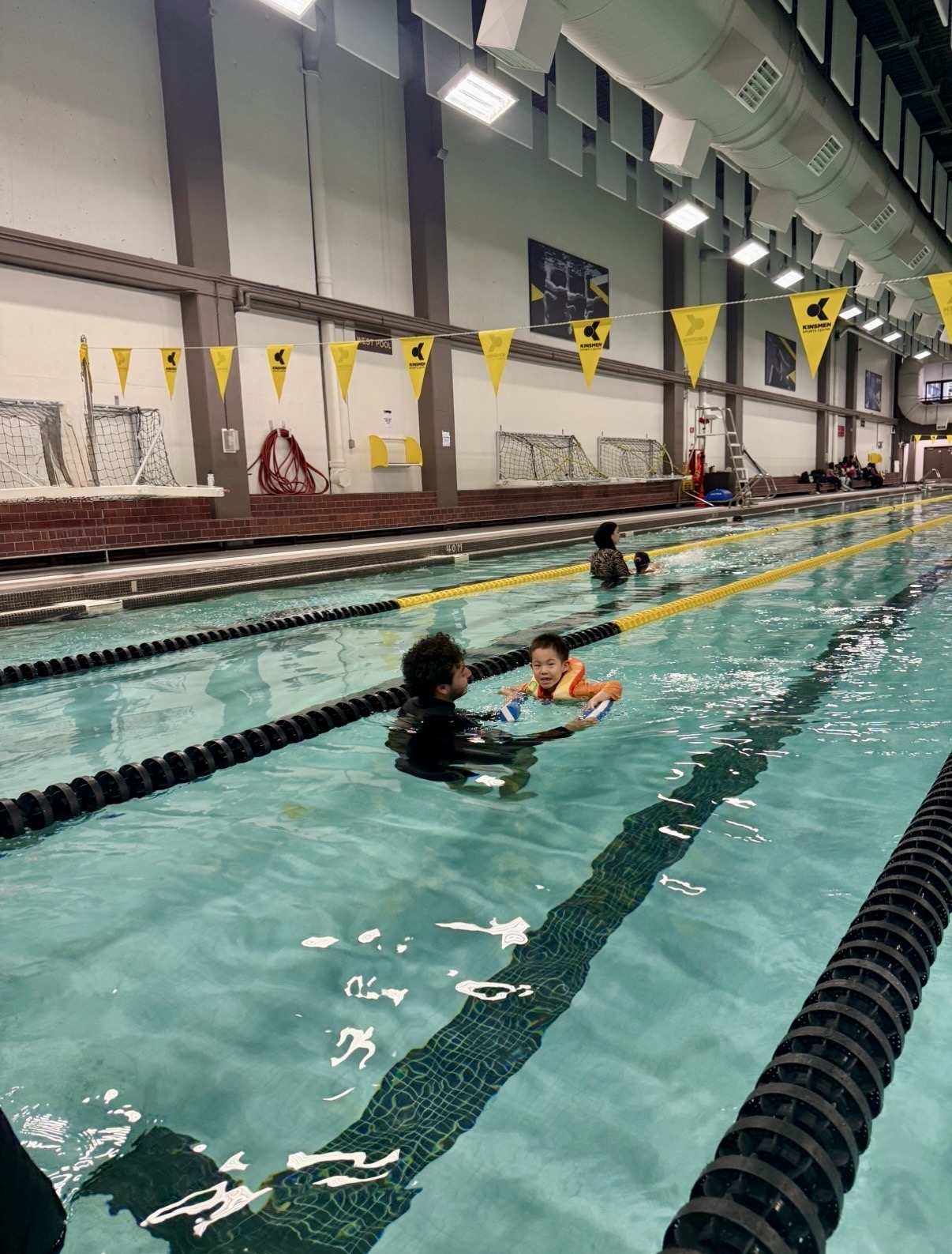 Volunteer instructor guiding a child with floaties through the pool lane at Kinsmen Sports Centre